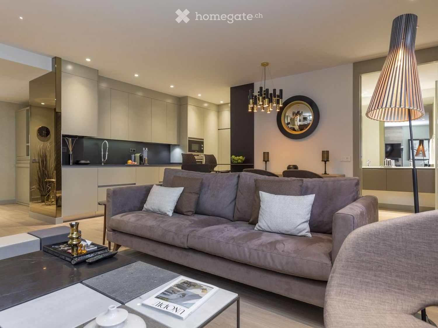 Modern living room with a grey sofa, coffee table, floor lamp, and a modern kitchen area with cabinets, a faucet, and a microwave.