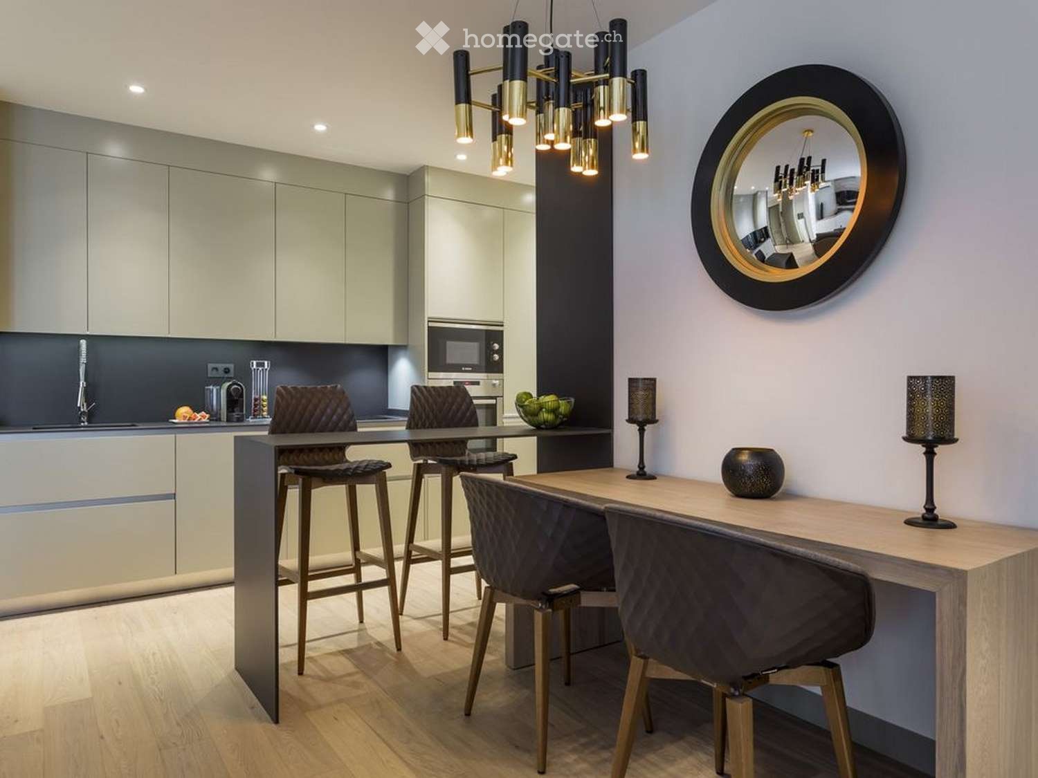 Modern kitchen and dining area with sleek cabinets, a central island, bar stools, and a round mirror on the wall.