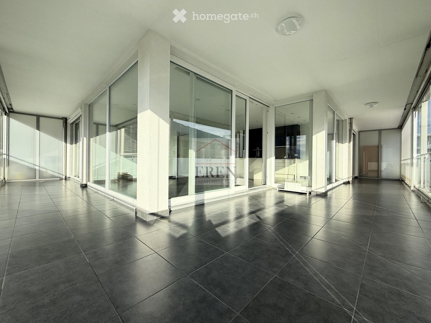 Empty room with large glass windows and polished tile flooring, featuring white walls and modern lighting fixtures.