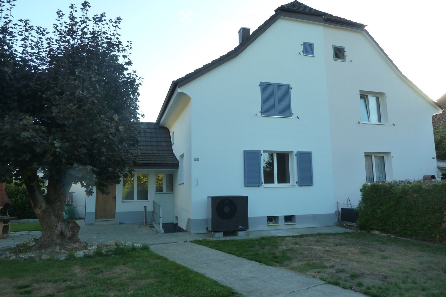 Two-story white house with blue shutters, a small porch, and an air conditioning unit on the side.