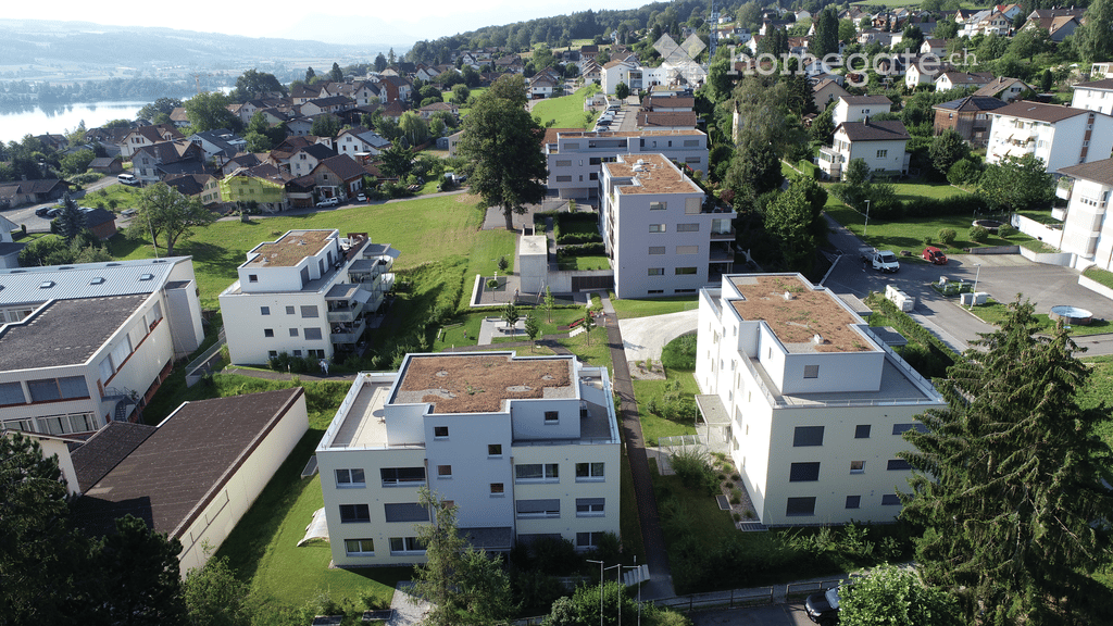 Aerial view of a residential area with multiple apartment buildings, green spaces, parking lots, and a swimming pool.