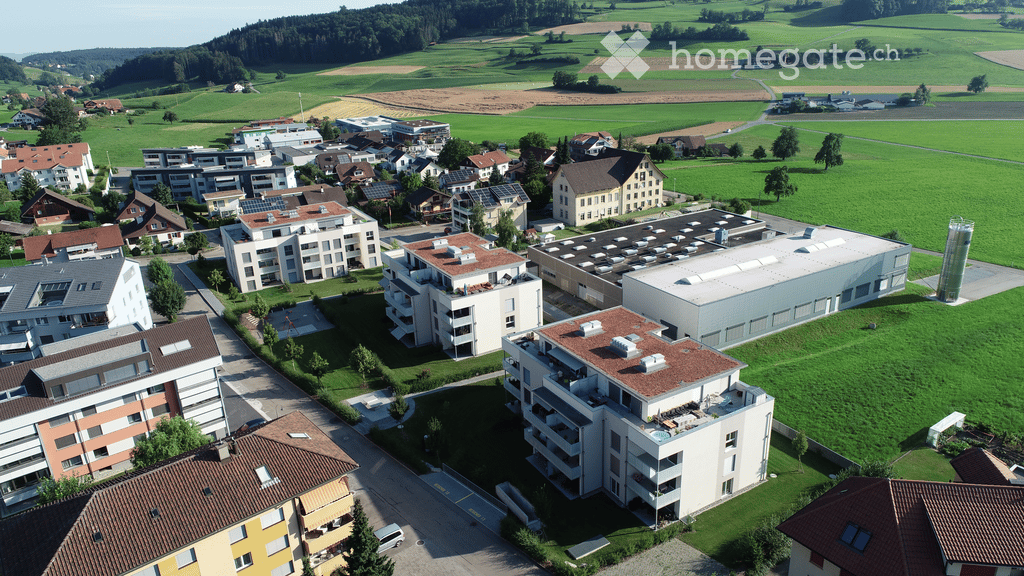 Aerial view of a residential area with multiple apartment buildings, surrounded by green fields and scattered trees.