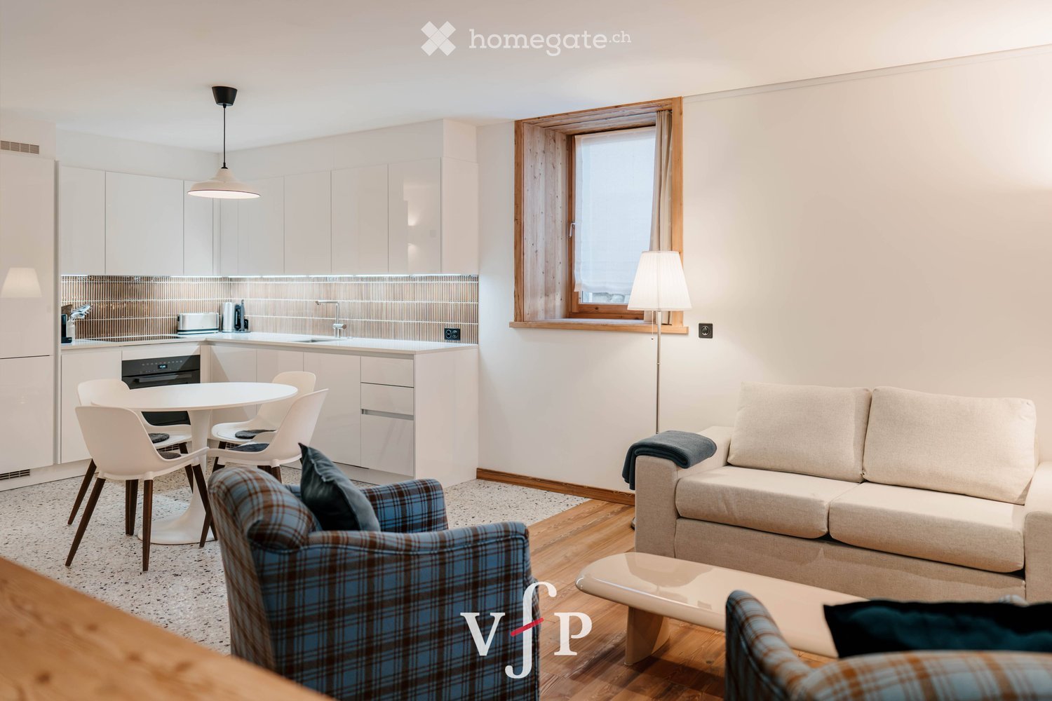Modern open-plan living and dining area with a sofa, armchair, coffee table, dining table with chairs, and a kitchen area with cabinets and an oven.