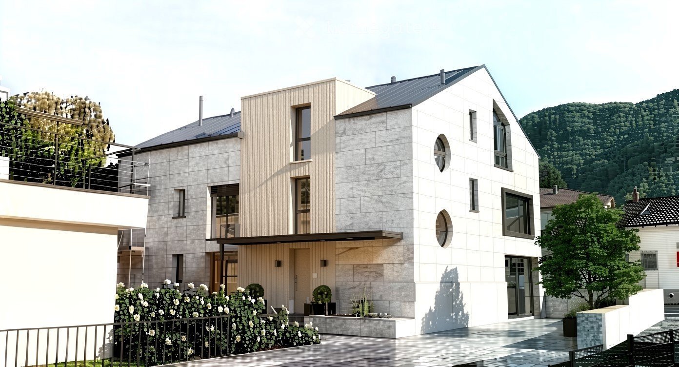 Modern two-story house with a combination of concrete and wood exterior, large windows, and a balcony with greenery. The house is surrounded by a landscaped garden with white flowers and shrubs, and there is a scenic mountain view in the background.