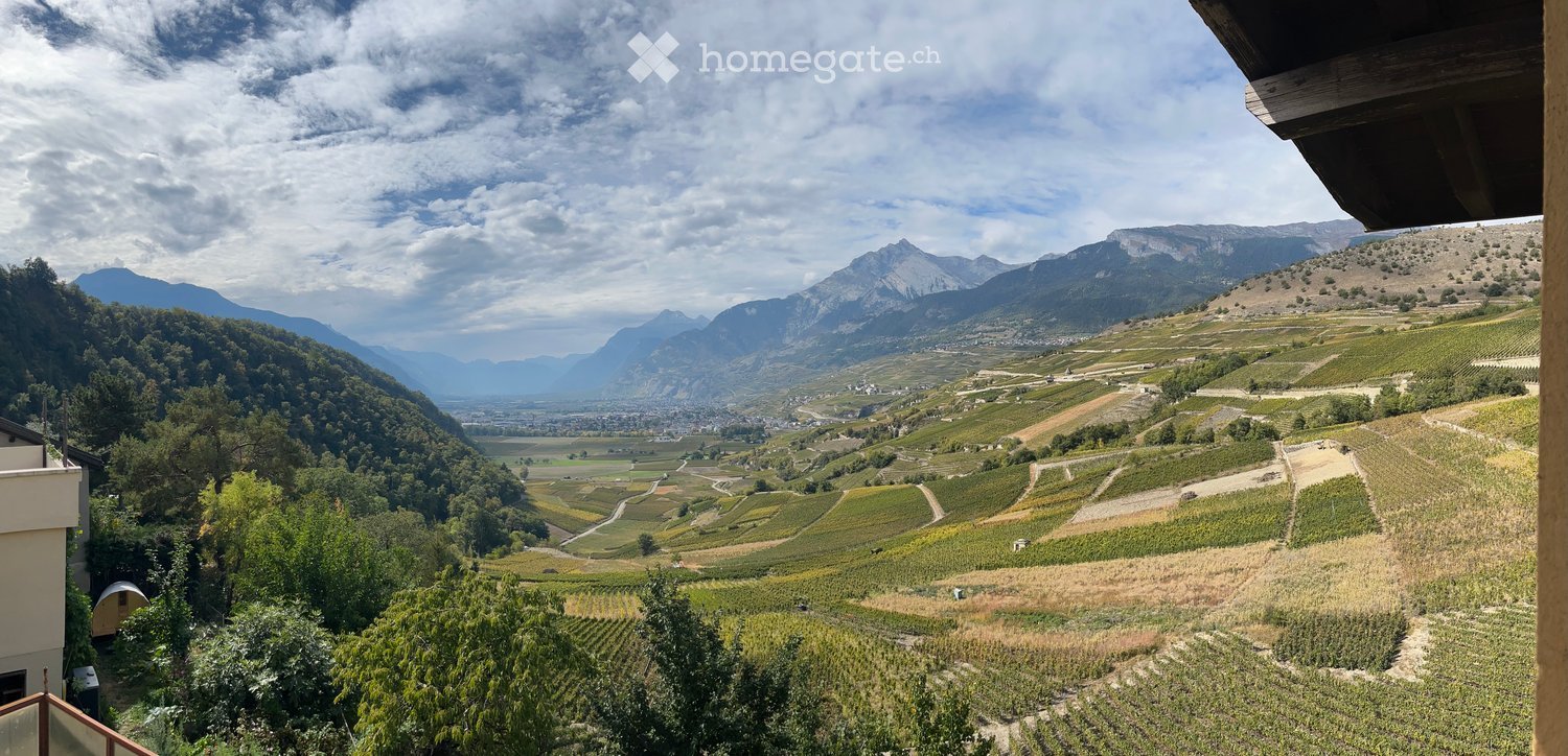 Balcony overlooking a scenic valley with vineyards, mountains, and a town in the distance.