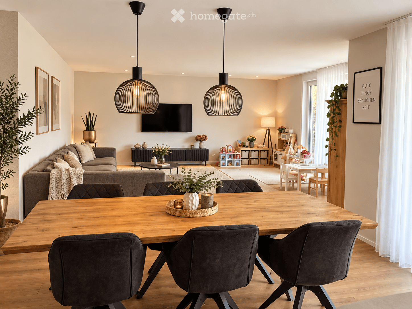 Bright, open living and dining area with wooden flooring, large windows, and modern decor. Features a grey sofa, wooden dining table with dark chairs, pendant lights, and decorative plants.