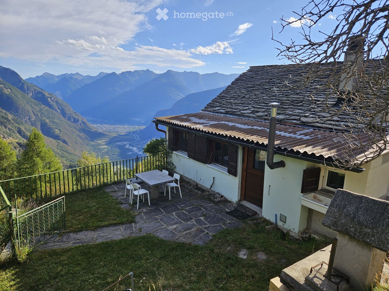 A small outdoor area with a table and chairs, overlooking a scenic mountain view.