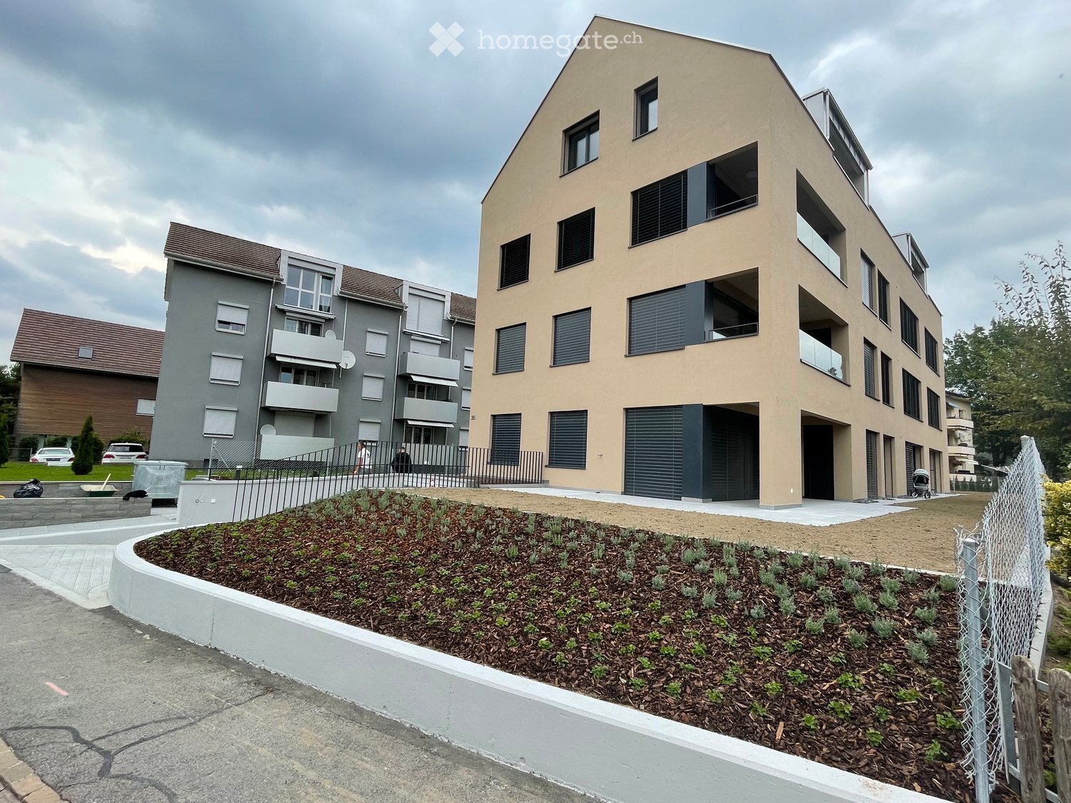 Two-story residential building with modern design, multiple windows, balconies, and a landscaped garden area in front.