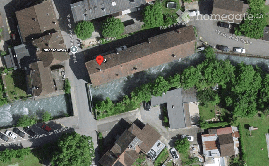 Aerial view of a residential area showing multiple buildings with red-tiled roofs, surrounded by greenery and streets.