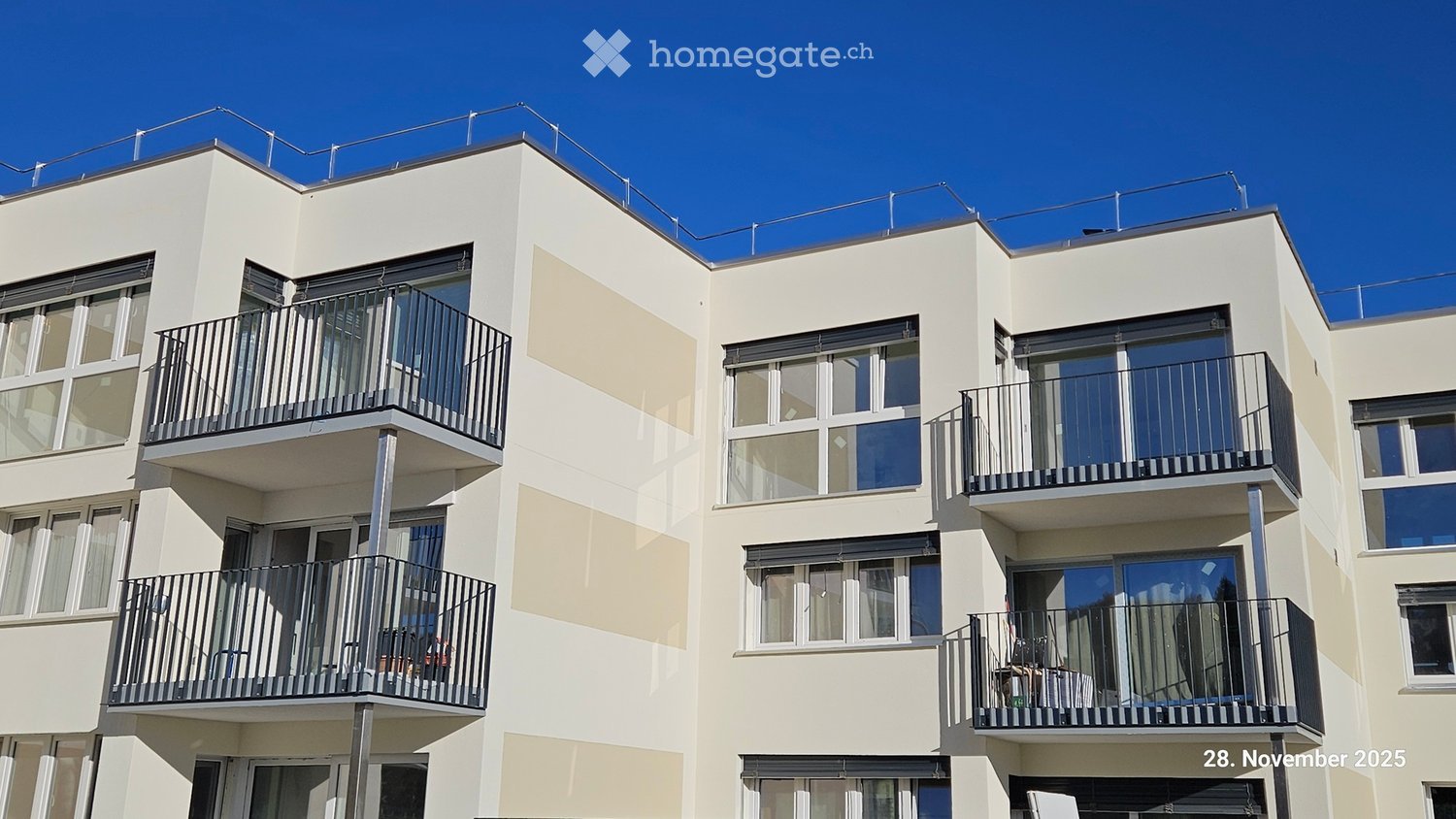 Modern 3-story building, beige facade, large glass windows, balconies on each floor