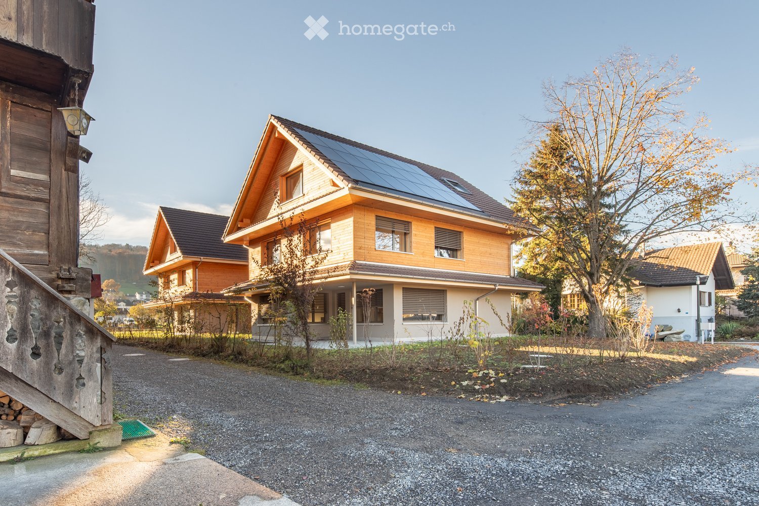 A modern two-story house with a wooden facade, solar panels on the roof, and a well-maintained garden area.