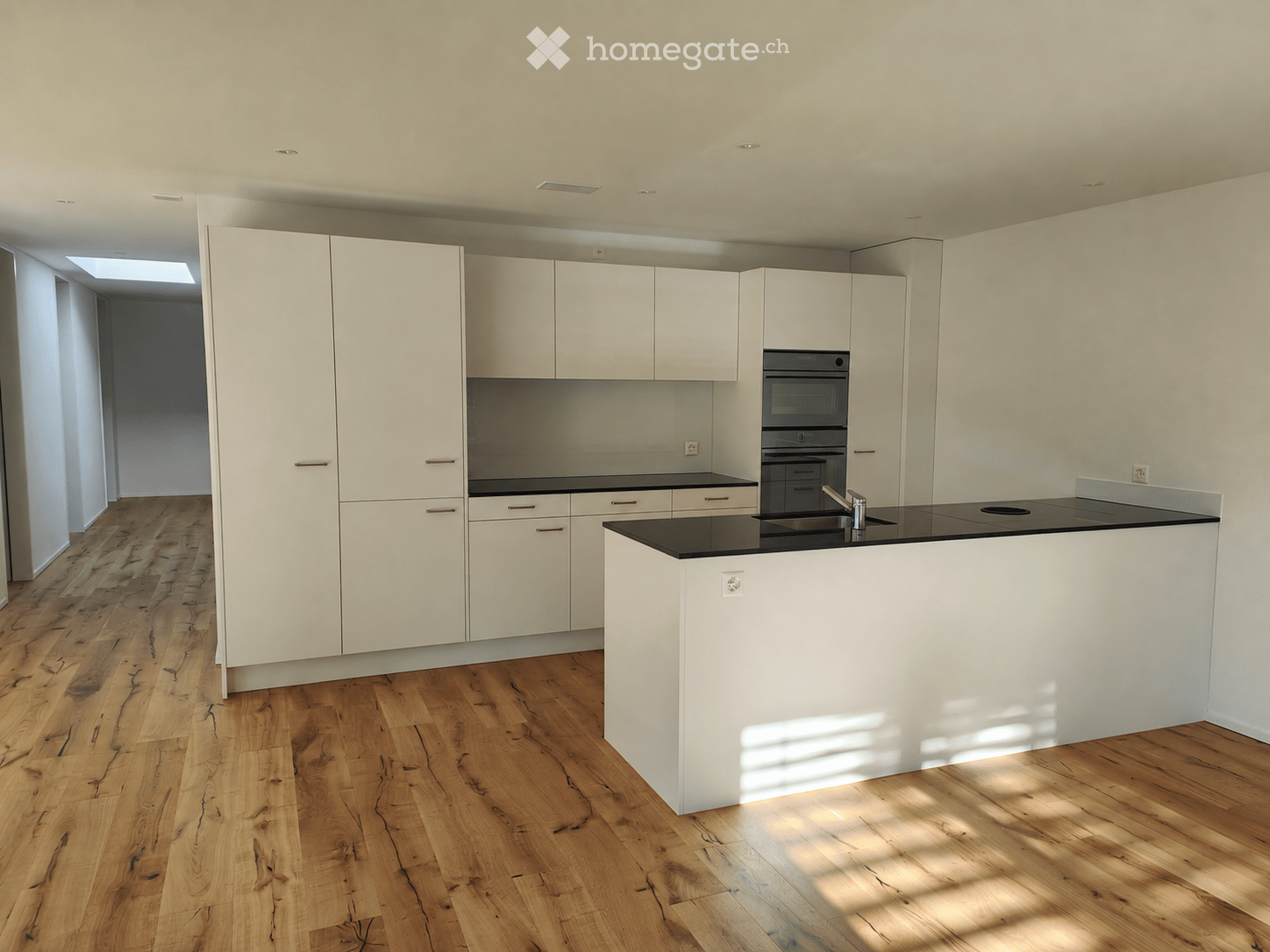 Modern kitchen with white cabinets, black countertops, and a central island. Features a wooden floor and built-in appliances.