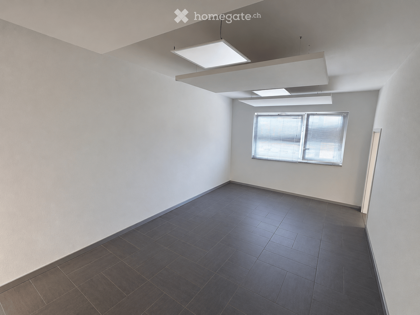 Empty room with white walls, dark tiled floor, large window with blinds, and modern ceiling lights.