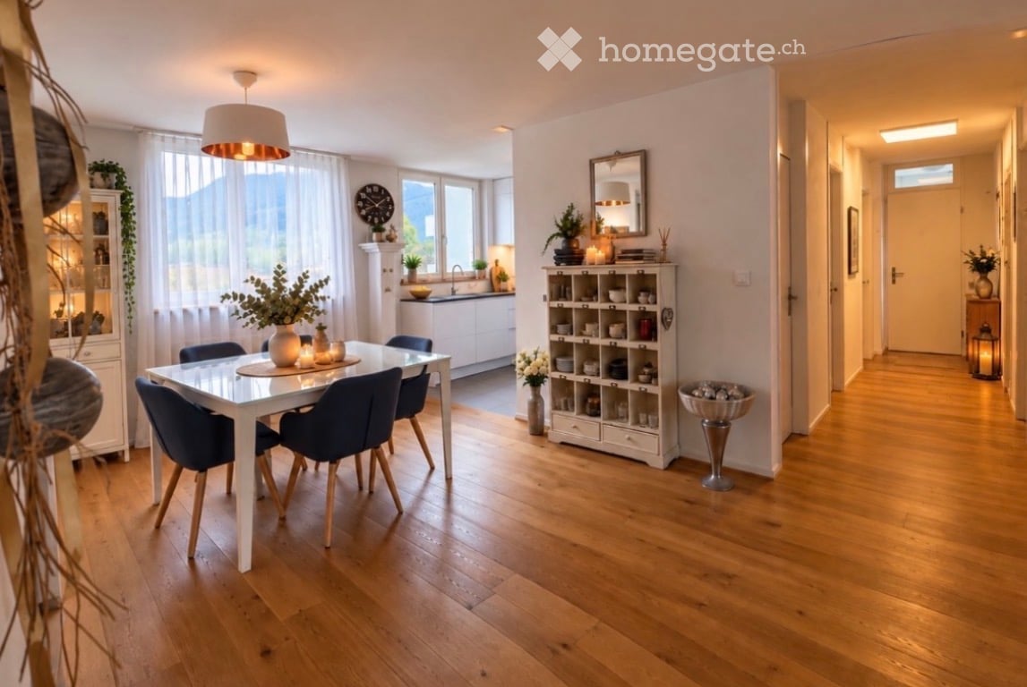 Bright dining area with a white dining table and four blue chairs, surrounded by wooden flooring and large windows. A white kitchen area is visible in the background with cabinets, a sink, and a faucet. Shelves and decorative items are placed around the r