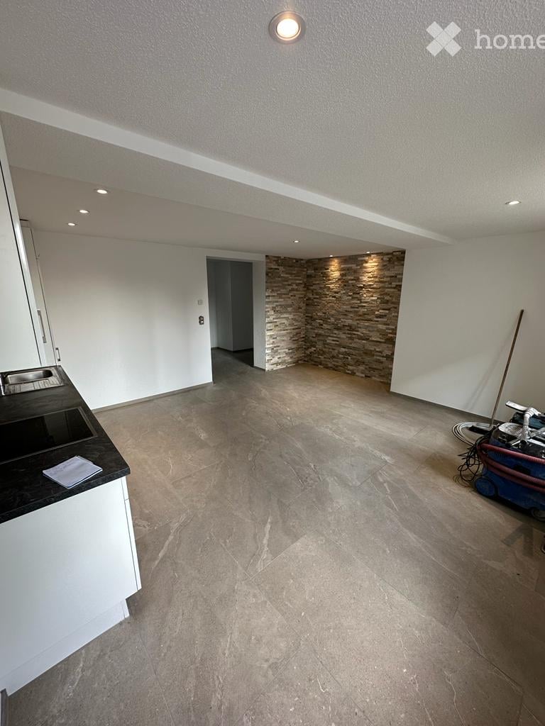 Empty room with white walls, tiled floor, and a small black countertop with a sink. A stone accent wall and a doorway lead to another space.