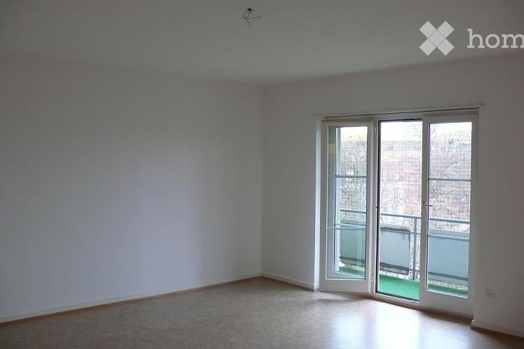 Empty room with light-colored walls, wooden floor, and large sliding glass doors leading to a balcony.