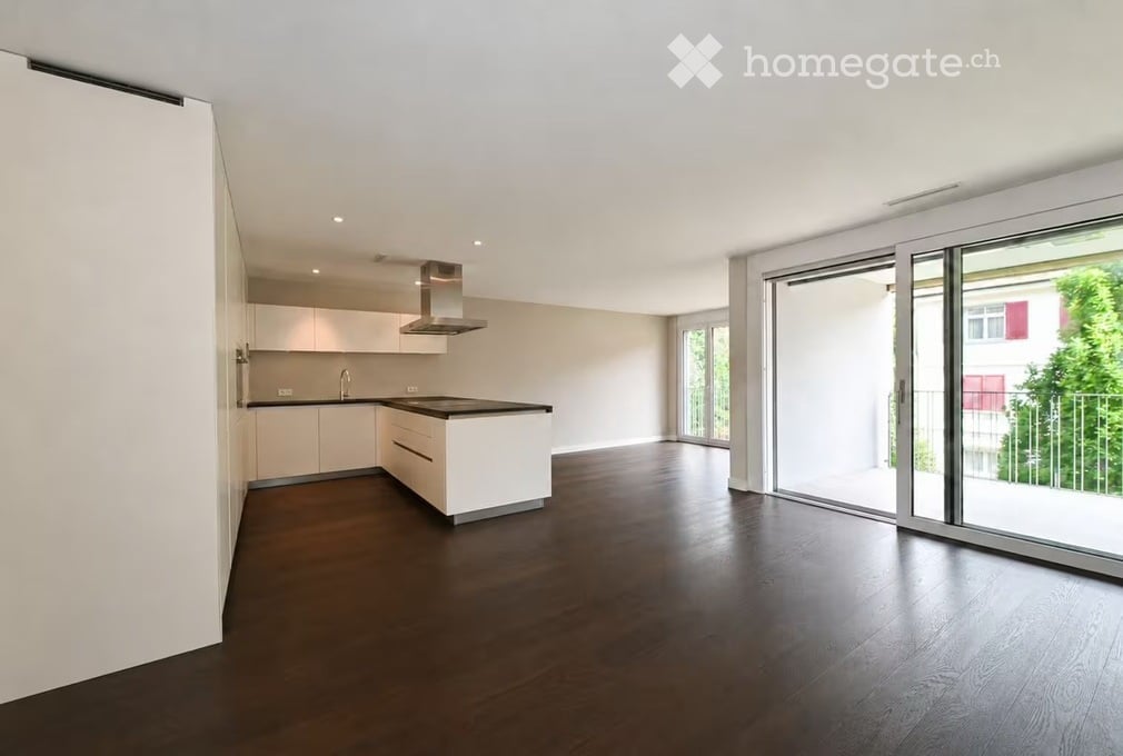 Modern kitchen with white cabinets, dark wooden floor, kitchen island, and large sliding glass doors leading to a balcony.
