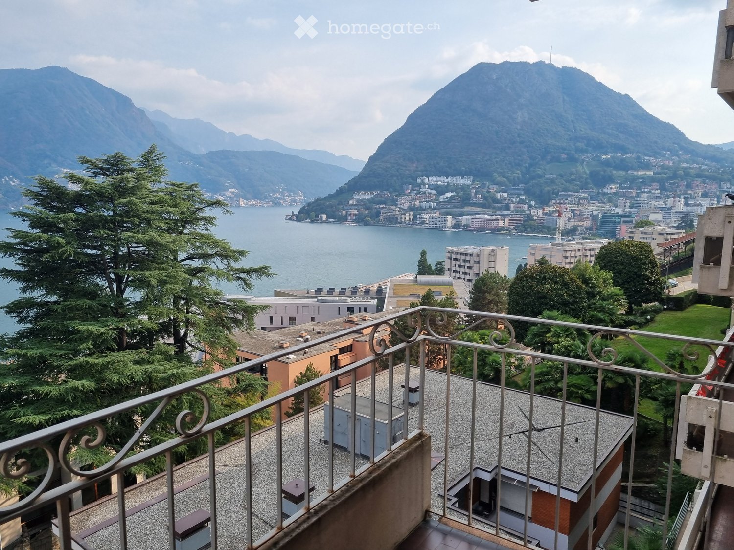 Balcony overlooking a scenic lake and mountain landscape, with a metal railing and tiled floor.