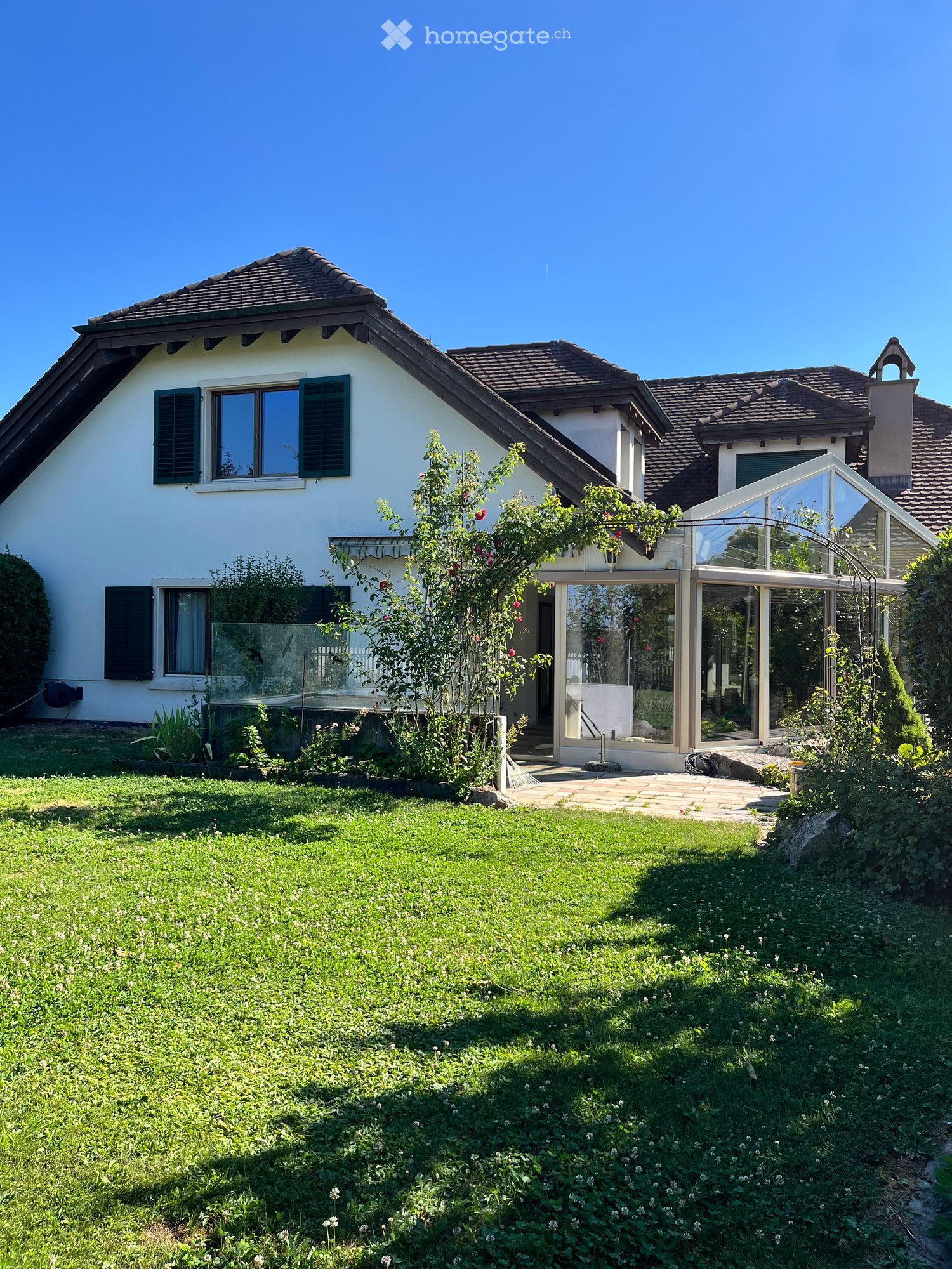 Two-story house with white exterior, green shutters, and a well-maintained garden with a patio area.