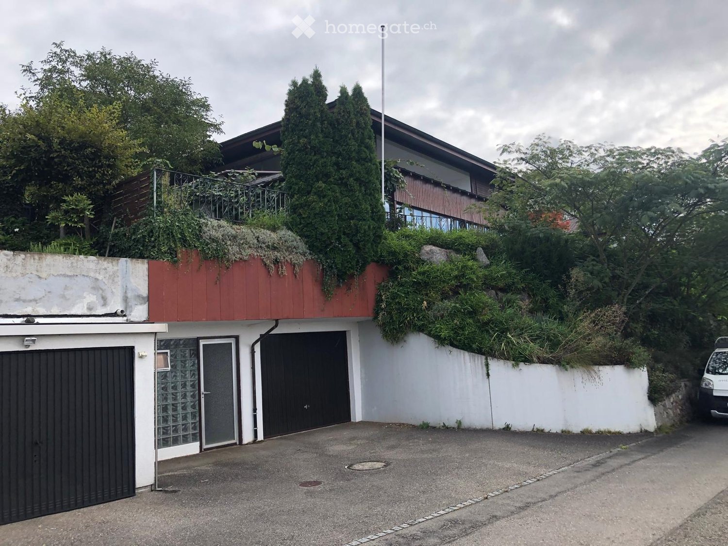 Two-story house with a red roof, white walls, garage, and greenery on the roof.