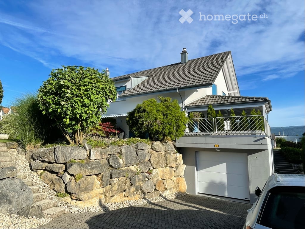 Two-story house with a garage, raised ground floor, and a balcony overlooking the garden.