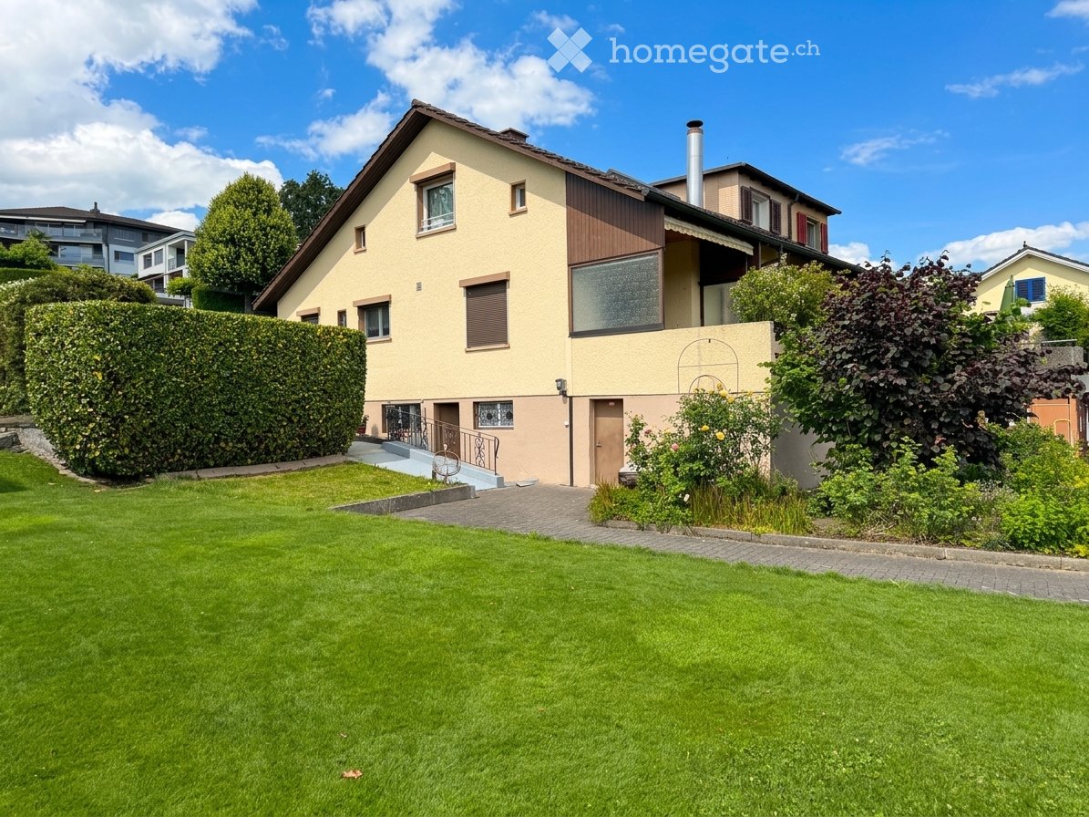 Two-story house with beige and brown exterior, multiple windows, a chimney, and a well-maintained lawn with surrounding greenery.