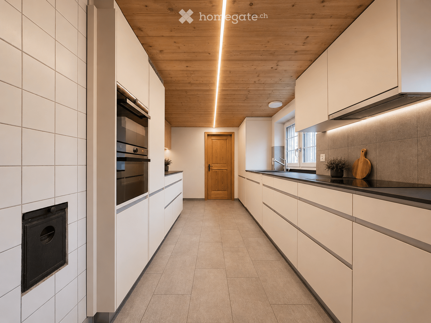 Modern kitchen with white cabinets, wooden ceiling, built-in oven, sink, and small potted plant on the counter.
