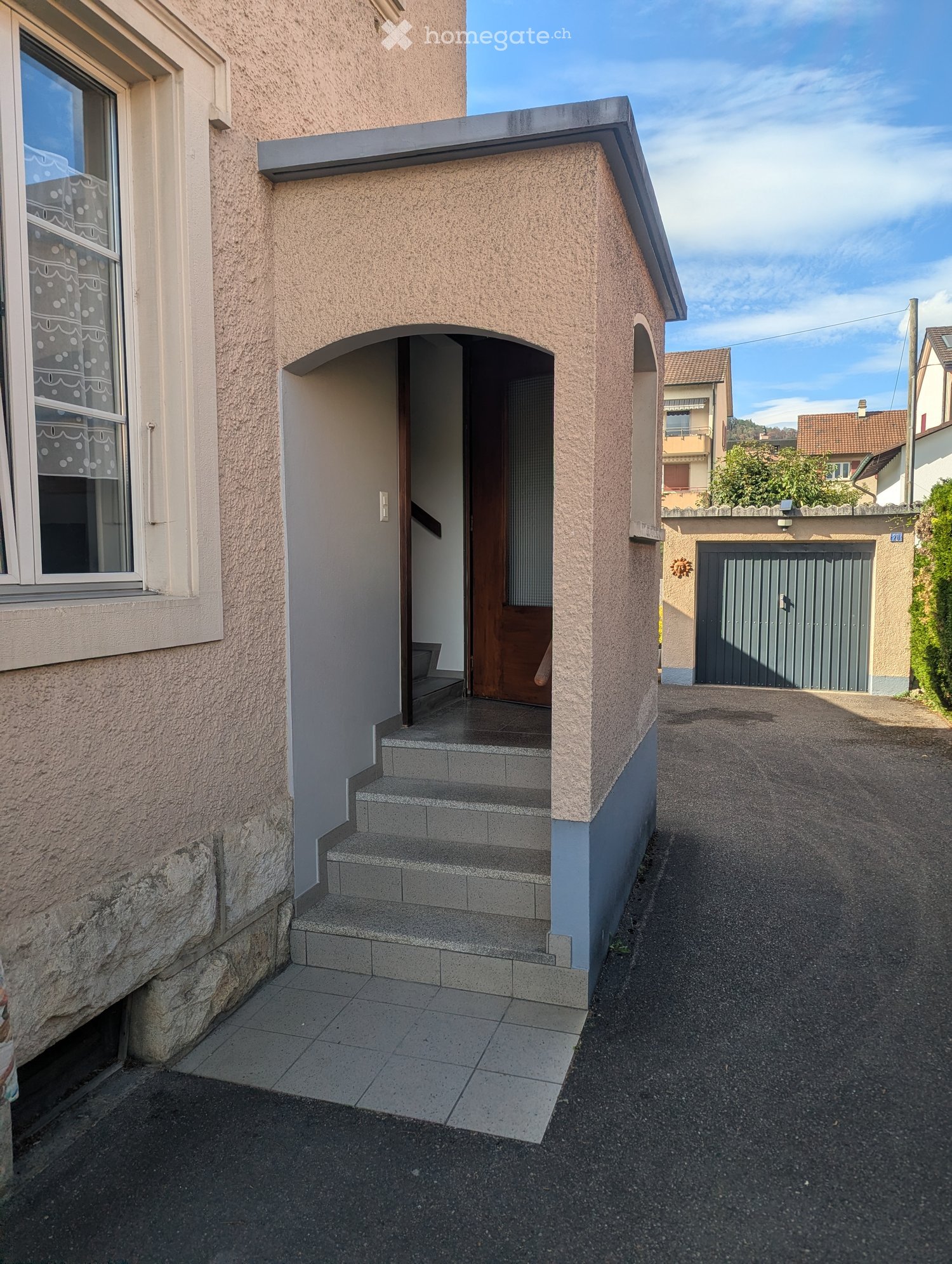 Entrance to a house with a small porch, steps, and a garage visible in the background.