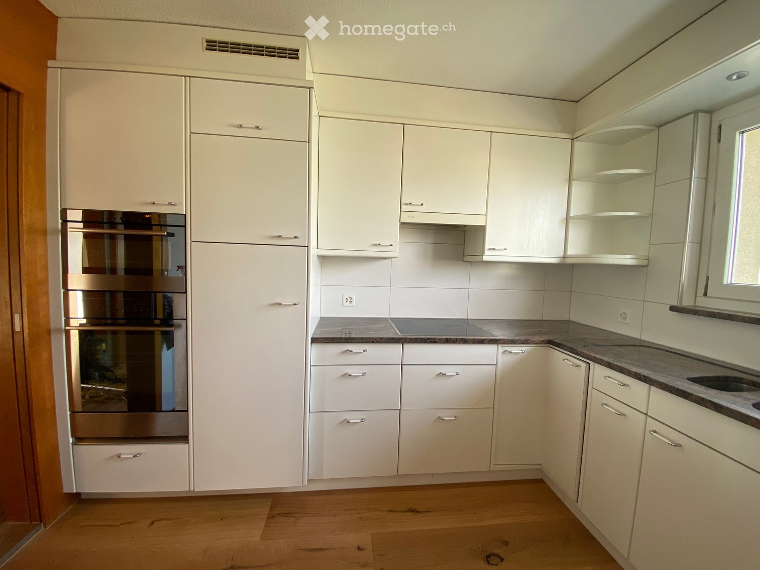 Modern kitchen with white cabinets, stainless steel oven, granite countertop, and wooden flooring.