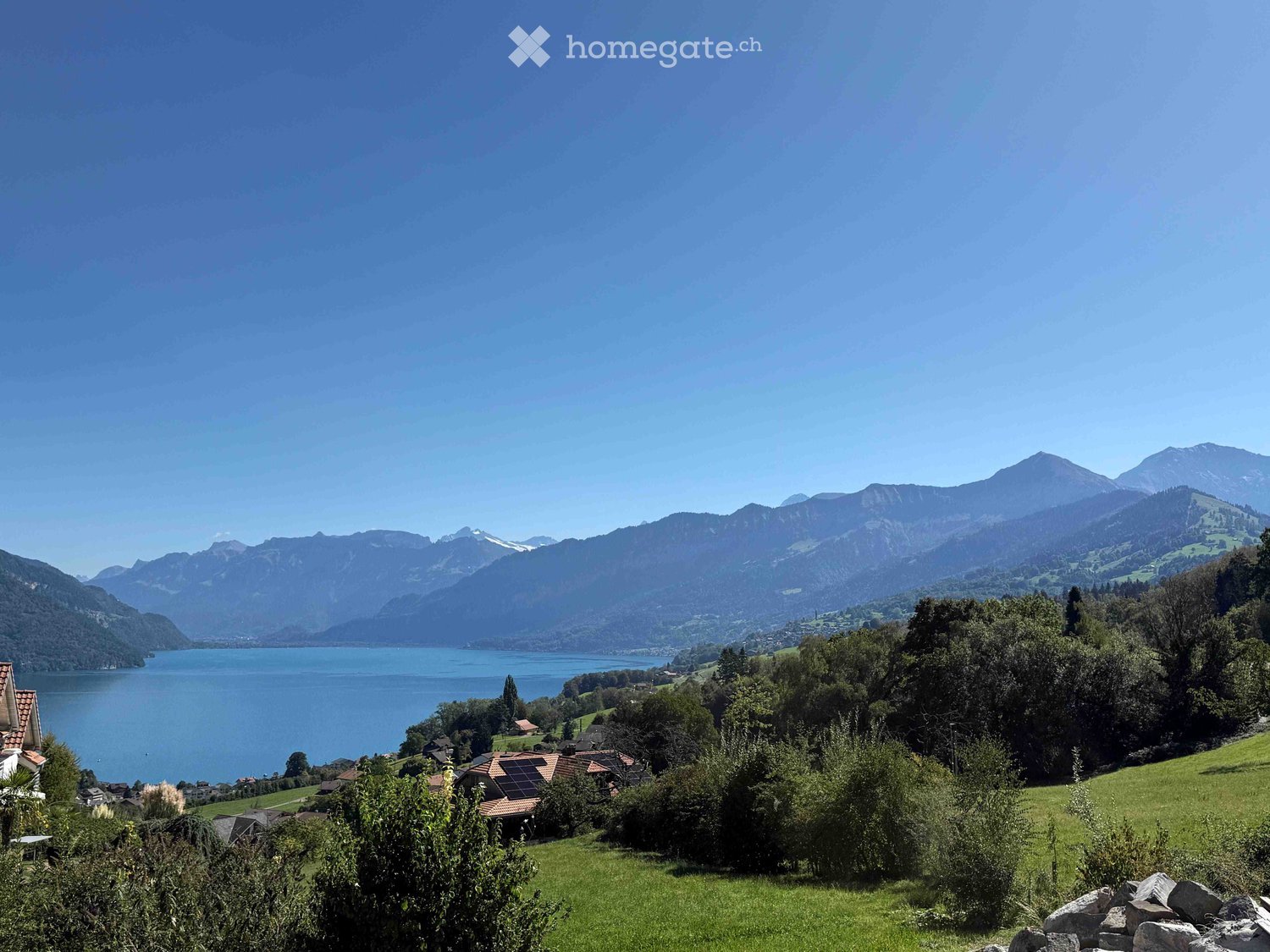 Scenic view of a lake surrounded by mountains, with a small village and green fields in the foreground.