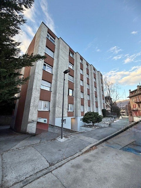 Multi-story residential building with a modern facade, featuring rectangular windows and brown shutters. The building is situated on a street with a sidewalk and streetlight.