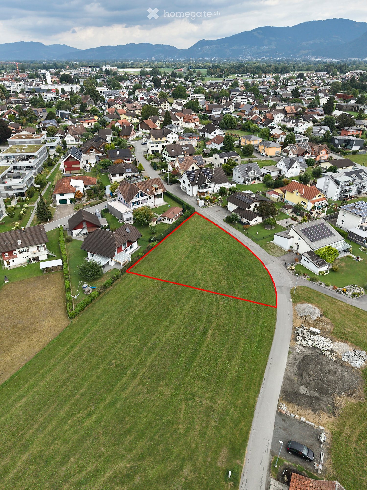 Aerial view of a suburban neighborhood with multiple houses, green lawns, and a highlighted plot of land outlined in red.