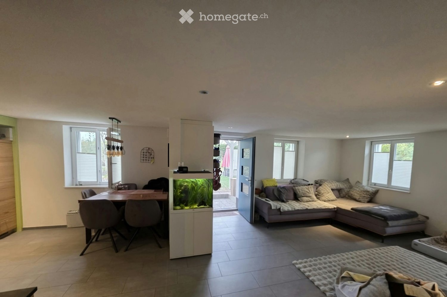 Modern living and dining area with a sectional sofa, dining table with chairs, fish tank, and decorative pillows.