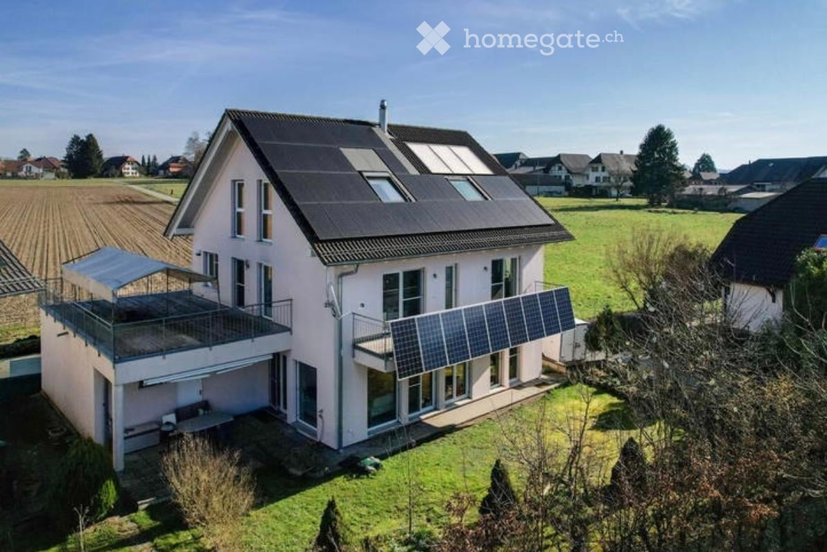 Two-story house with solar panels on the roof, balconies, and a covered outdoor seating area.