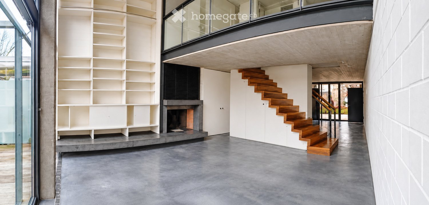 Modern hallway with concrete floors, white walls, built-in shelving, wooden staircase, and a fireplace.