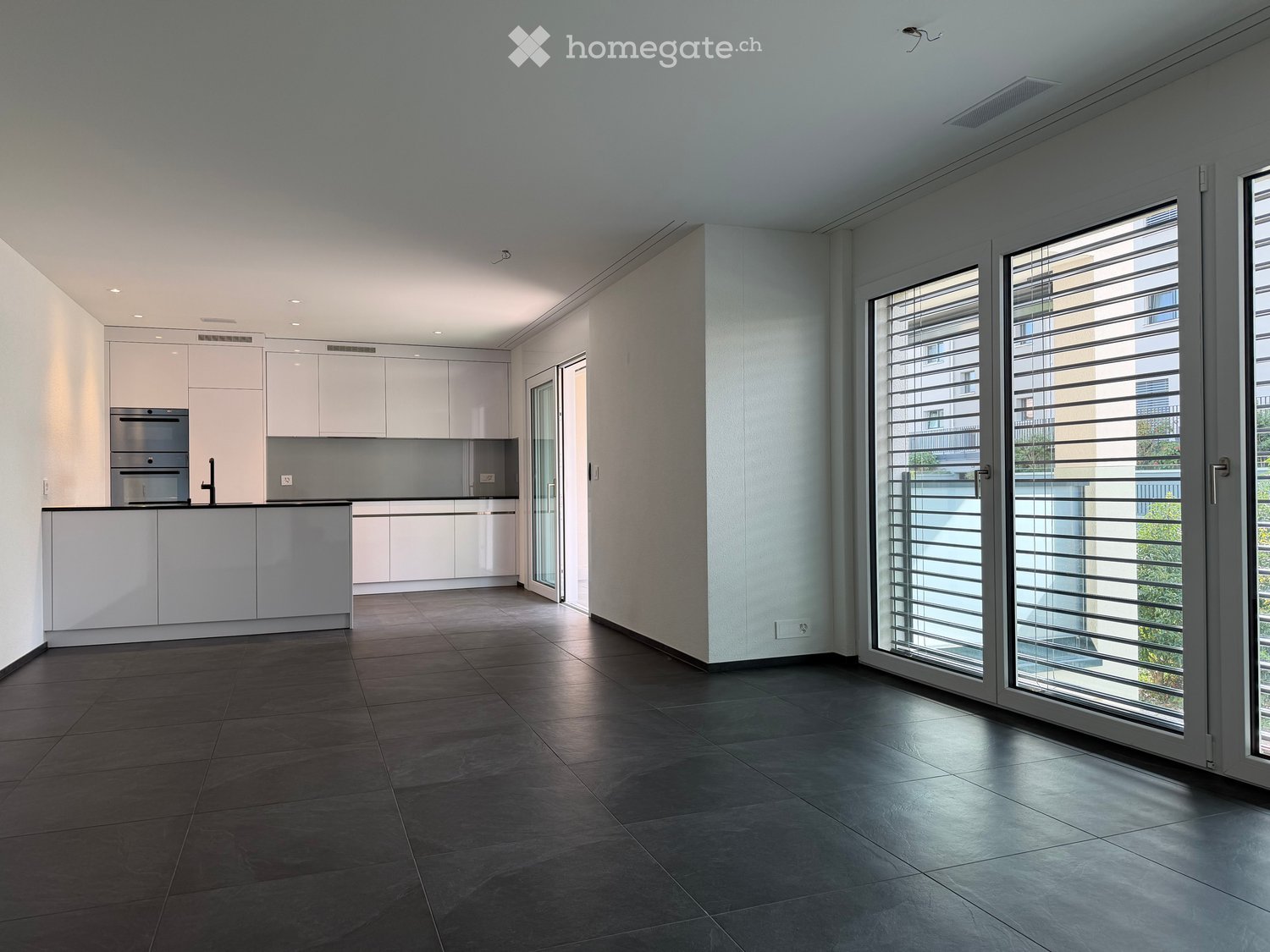 Modern kitchen with white cabinets, stainless steel appliances, dark tiled floor, and large sliding glass doors leading to a balcony.