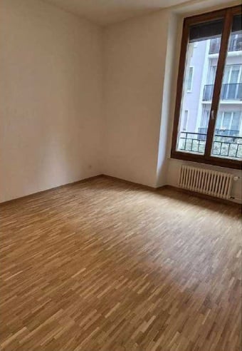Empty room with wooden flooring, white walls, and a large window with a radiator below it.
