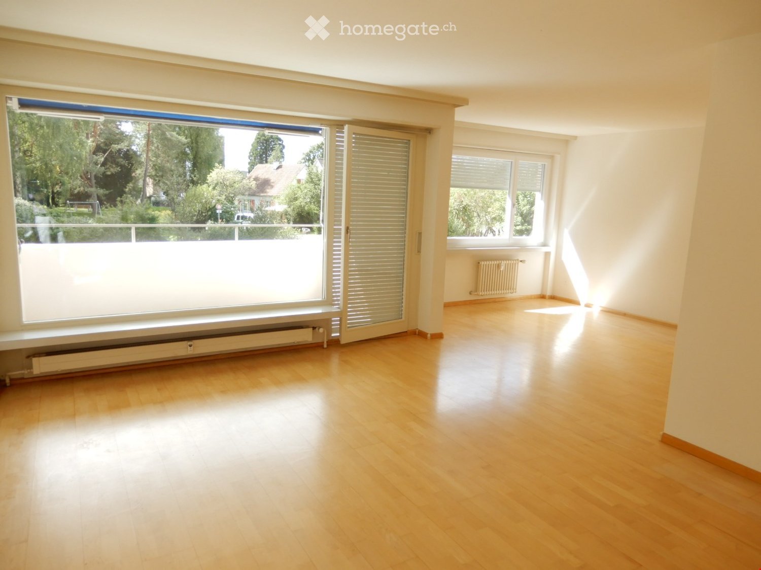 Empty room with wooden flooring, large windows, and radiators. No furniture or equipment present.