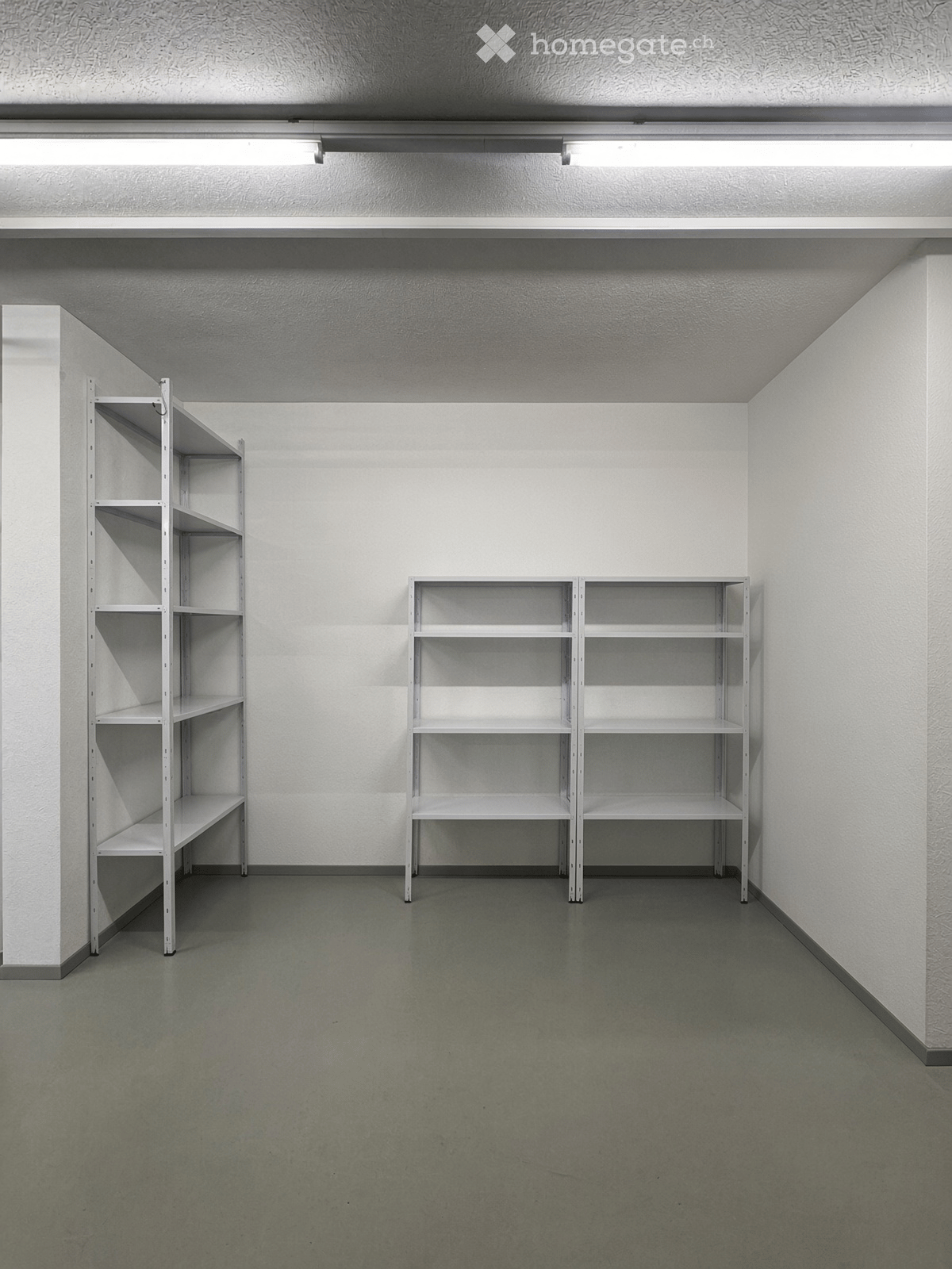 Empty room with white walls, grey floor, and two white metal shelving units.