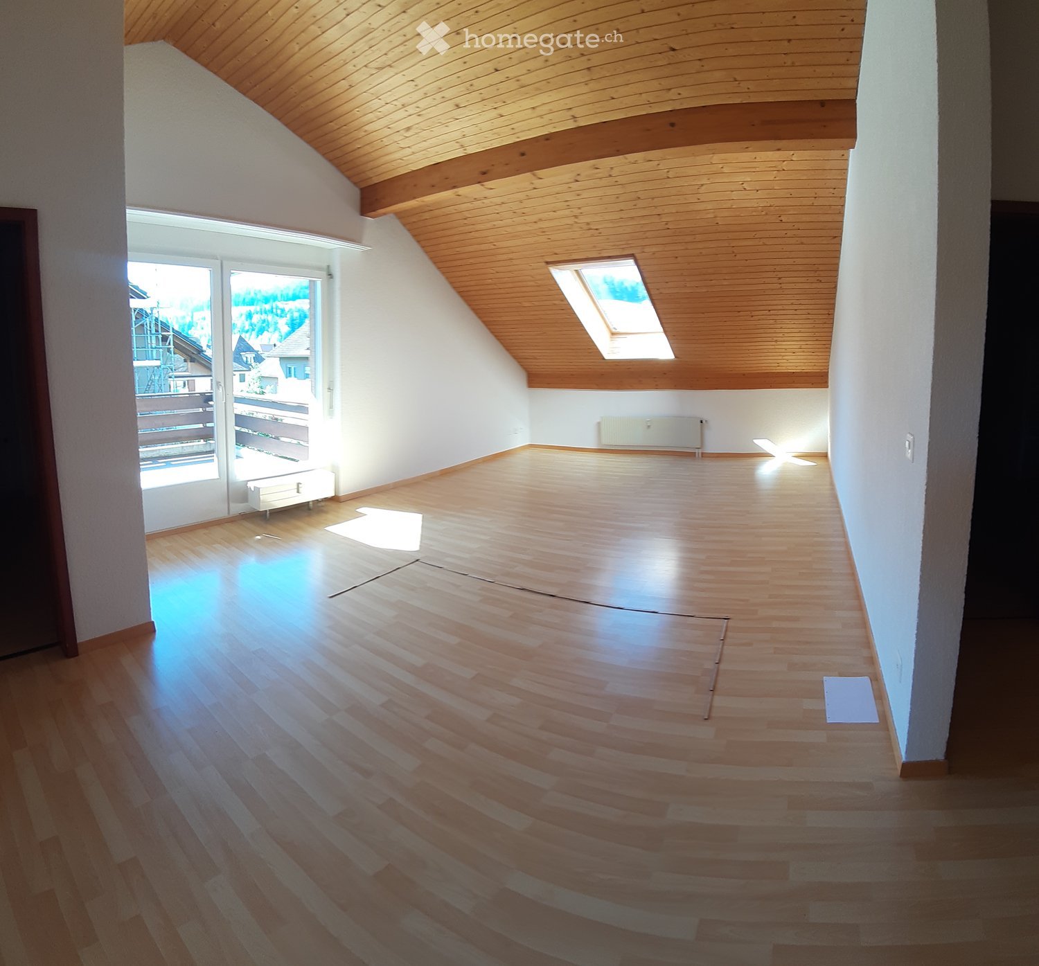 Empty room with wooden flooring, slanted wooden ceiling, large window, and skylight. No furniture or equipment present.