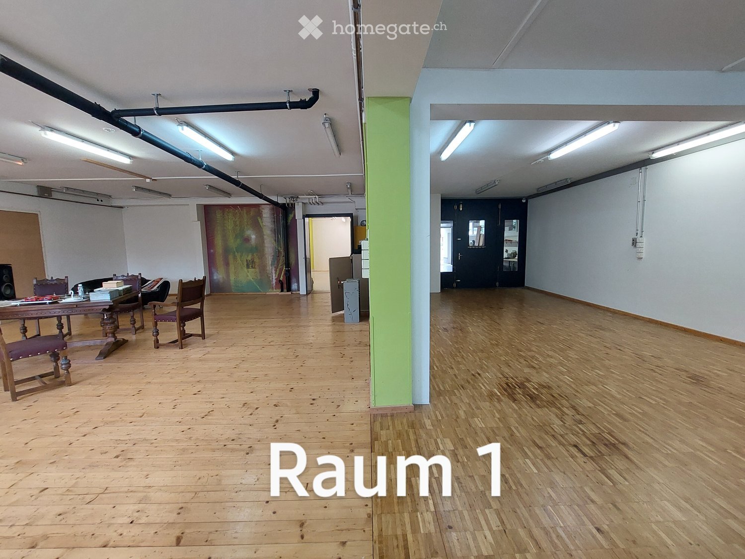 wooden floor, white walls, multiple fluorescent lights, table, chairs, large painting, central column, doors leading to other rooms