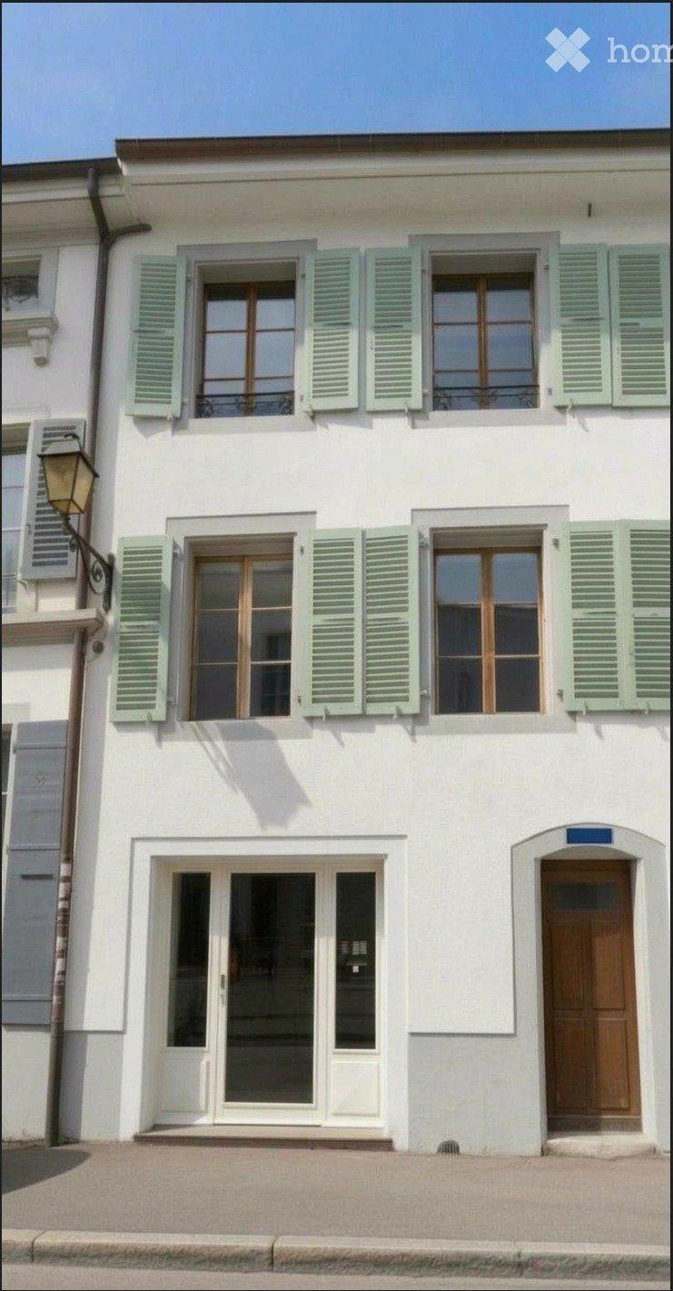 A two-story white building with green shutters, large windows, and a wooden front door.