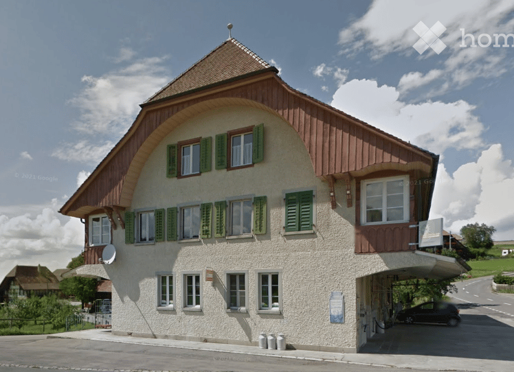Traditional Swiss-style building with a pitched roof, green shutters, and a covered garage entrance.