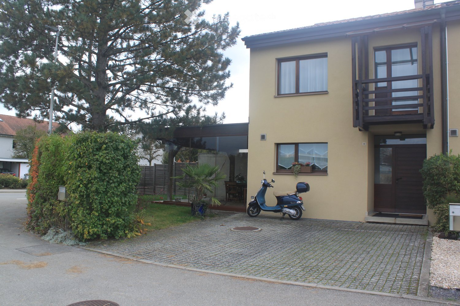Two-story house with beige exterior, large windows, balcony, and a scooter parked in front.