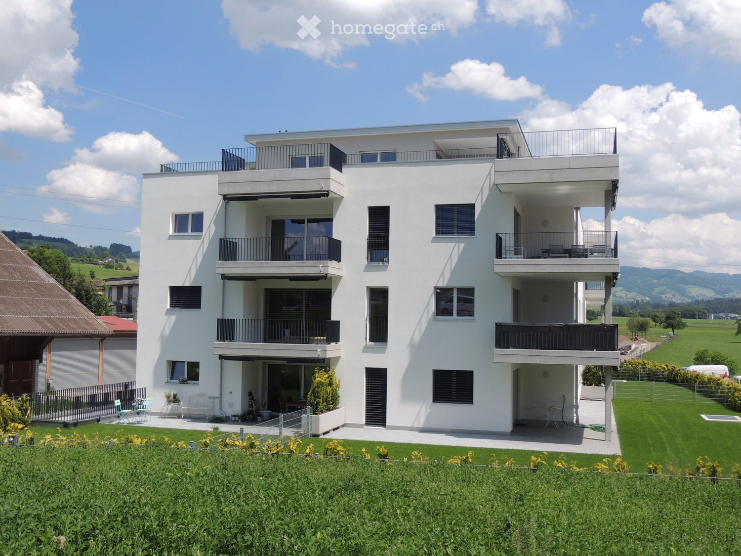 Modern two-story white house with multiple balconies, large windows, and a well-maintained lawn in front.