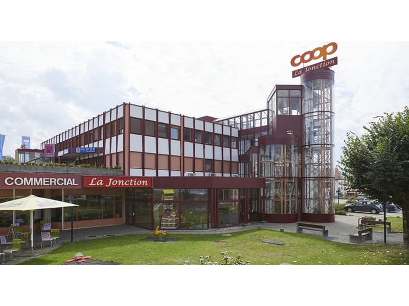 Commercial building, large glass windows, multiple floors, parking area, exterior seating, decorative signboard