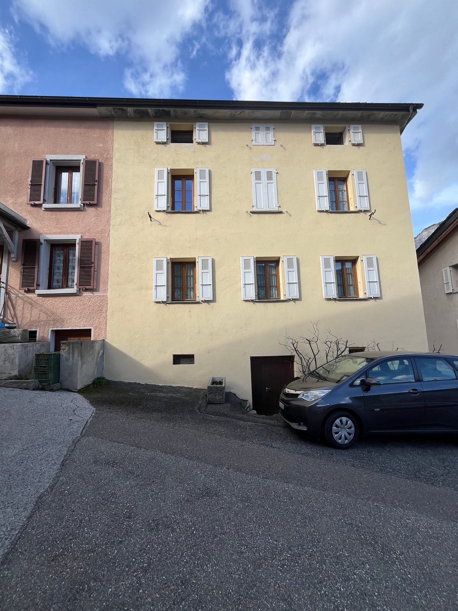 3 story house, beige walls, white shutters, car parked in front