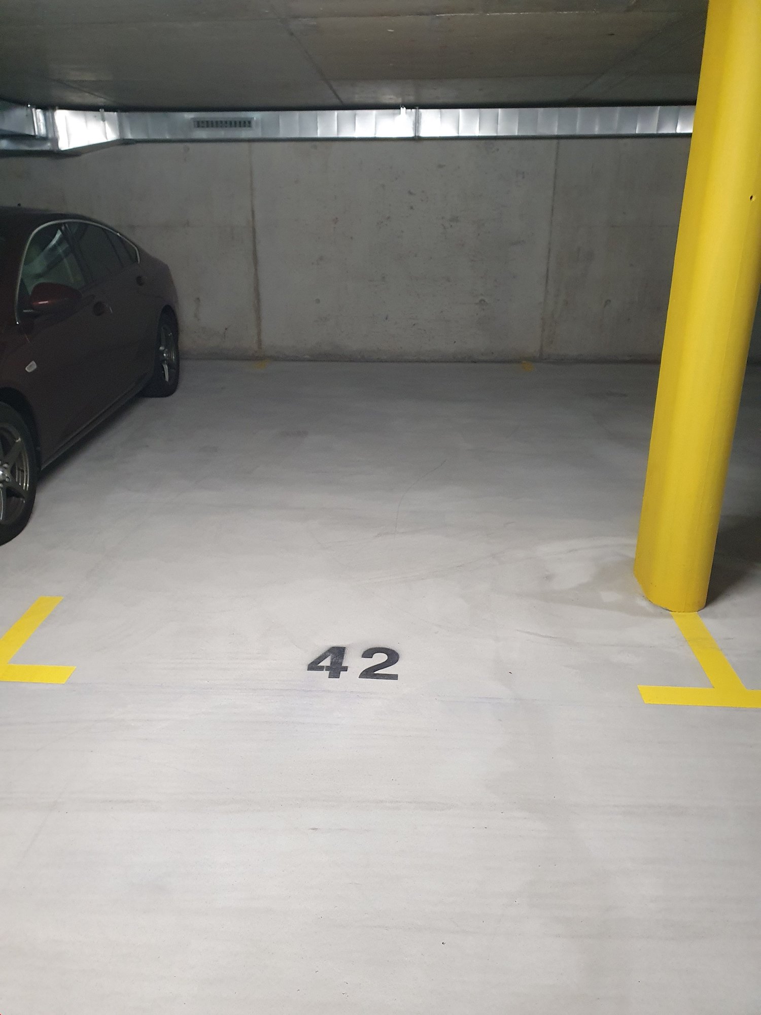 underground parking lot, with grey floor, white walls, yellow lines, car parking spot