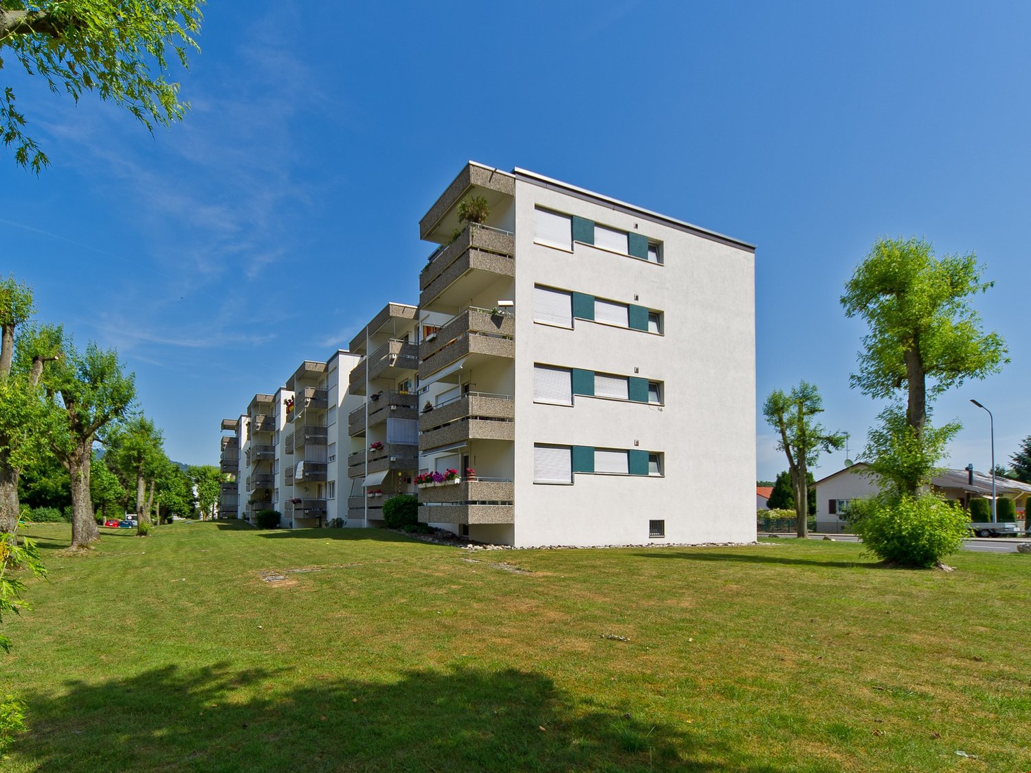 modern residential building, multiple balconies, white exterior, surrounding greenery, multiple stories