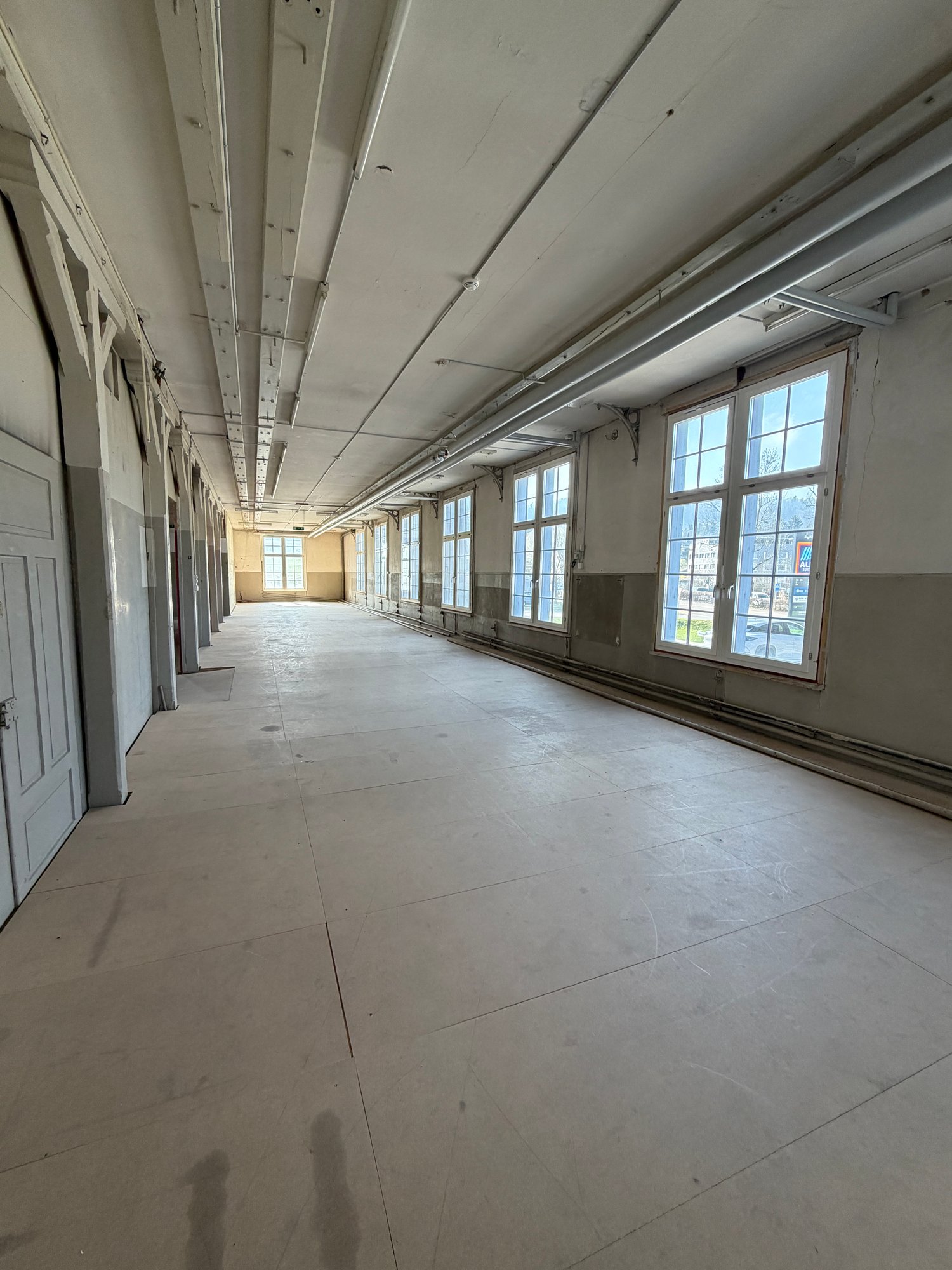 Empty room with white walls, ceiling, and floor, large windows, and doors on the left side